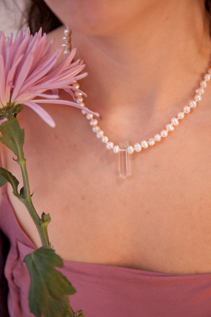 Cuello de mujer con una flor rosa, llevando el collar Venus, una joya artesanal confeccionada a mano en nuestro estudio con perlas auténticas y cuarzo blanco. 