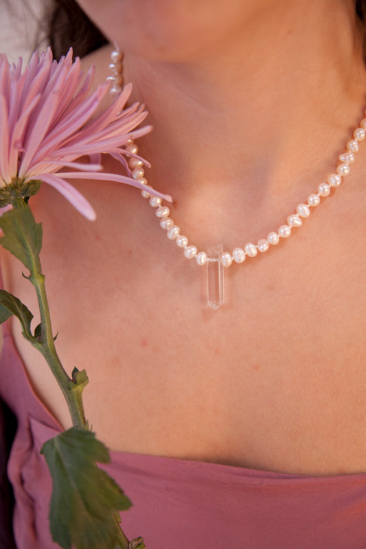 Cuello de mujer con una flor rosa, llevando el collar Venus, una joya artesanal confeccionada a mano en nuestro estudio con perlas auténticas y cuarzo blanco. 