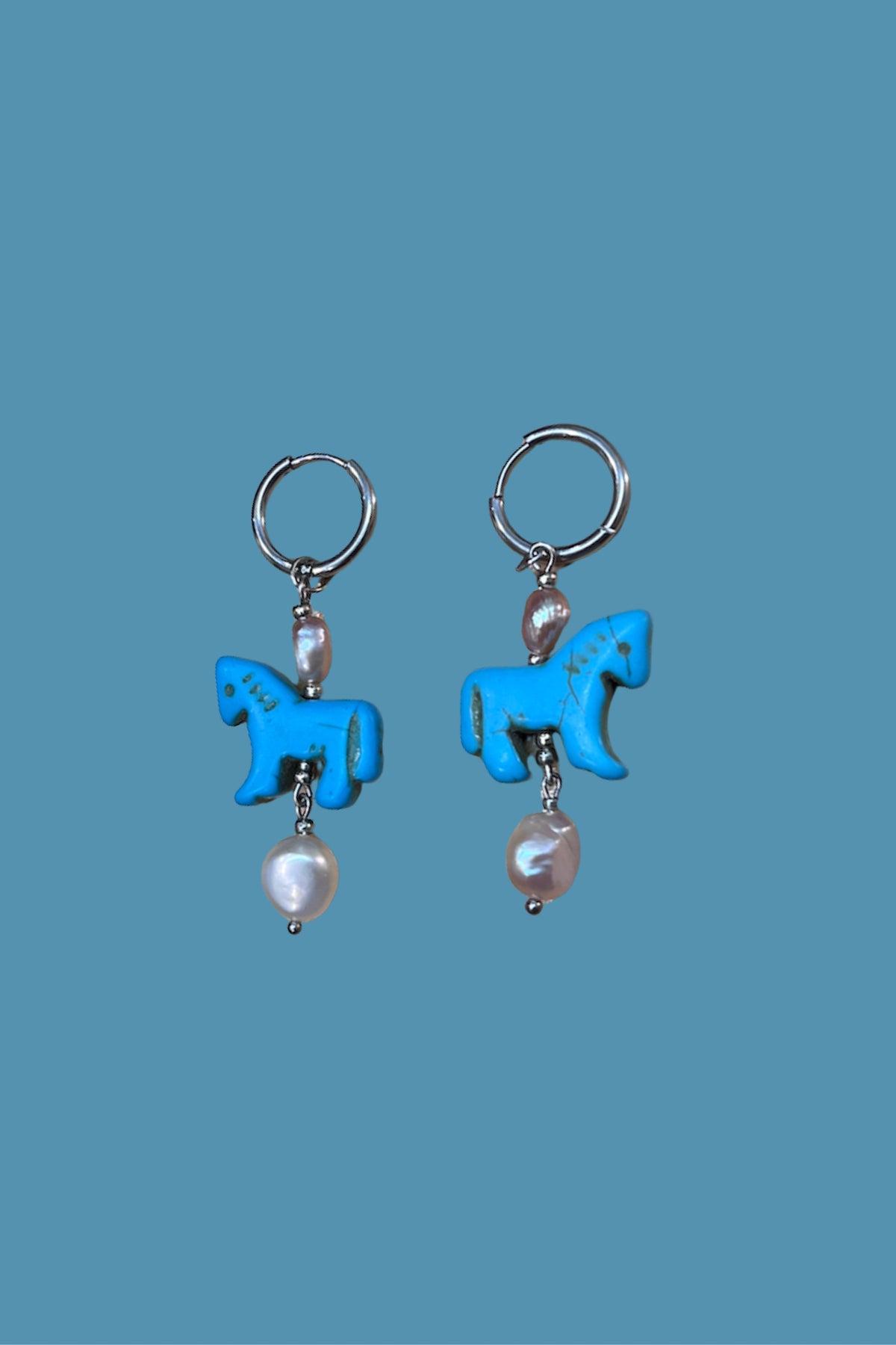 Pendientes artesanales de acero plateado y perlas que capturan la elegancia del año del caballo. 